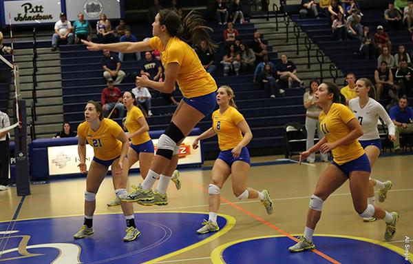 Pitt-Johnstown’s red shirt junior outside-hitter Marissa Erminio in the air with a spike as teammates watch the play develop.