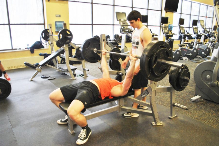 Senior+Ethan+Qualters+lifts+weight+on+the+bench+press+as+junior+Nick+Esola+spots+him+in+the+Wellness+Center+on+Friday.